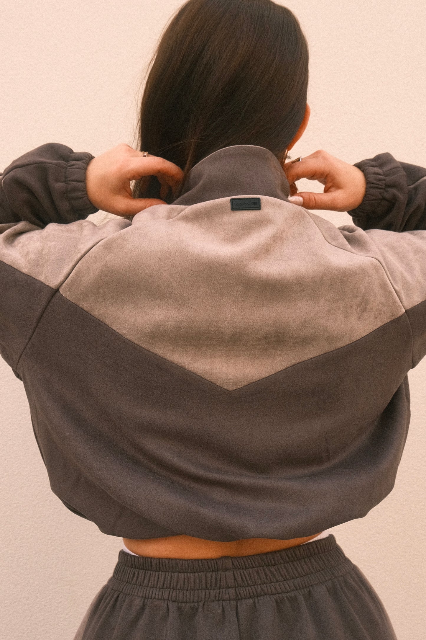 Cropped grey women’s streetwear jacket with front zipper, side pockets, and unique geometric cutouts on the back – relaxed fit and soft brushed fabric.