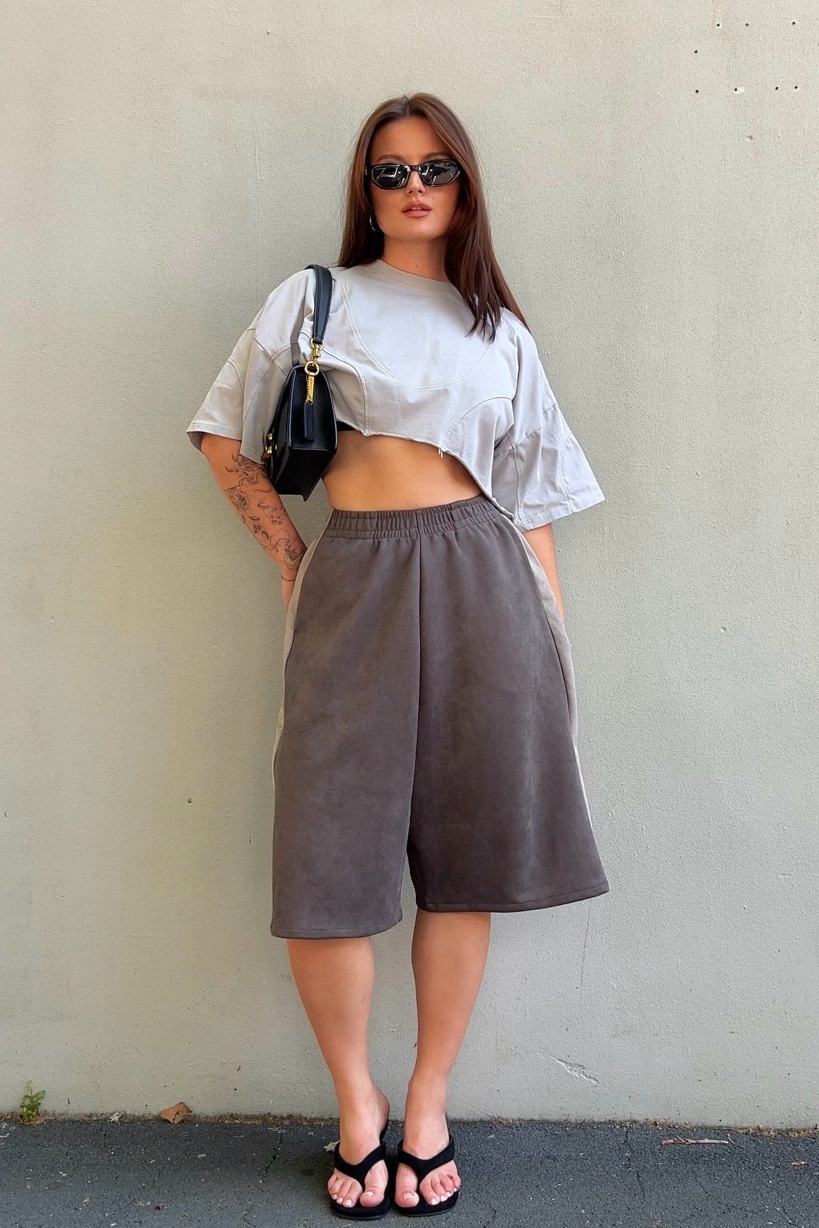 Woman wearing a white crop top and brown wide-leg pants against a plain wall.