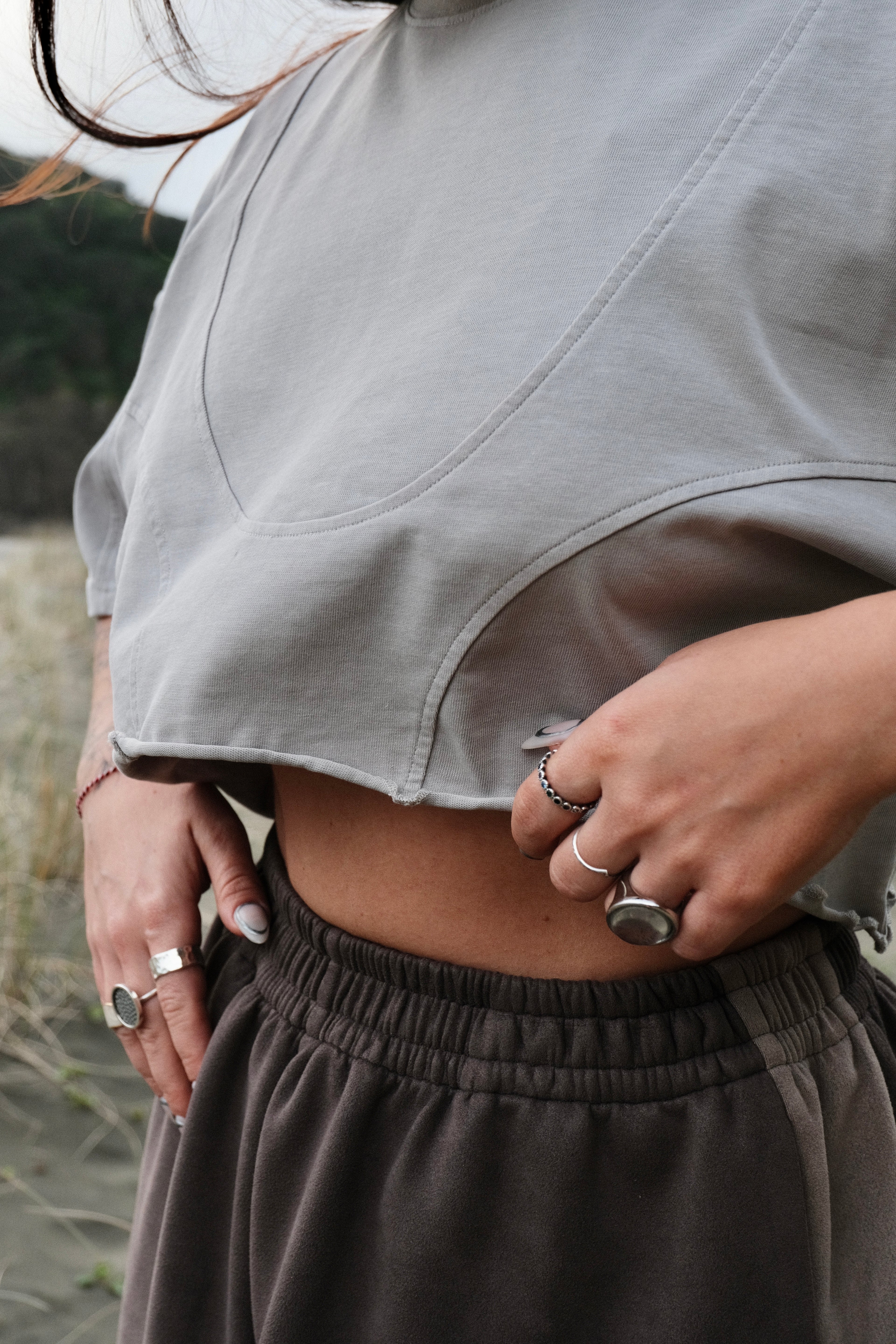 Person wearing a gray cropped top and grey pants with visible jewelry.