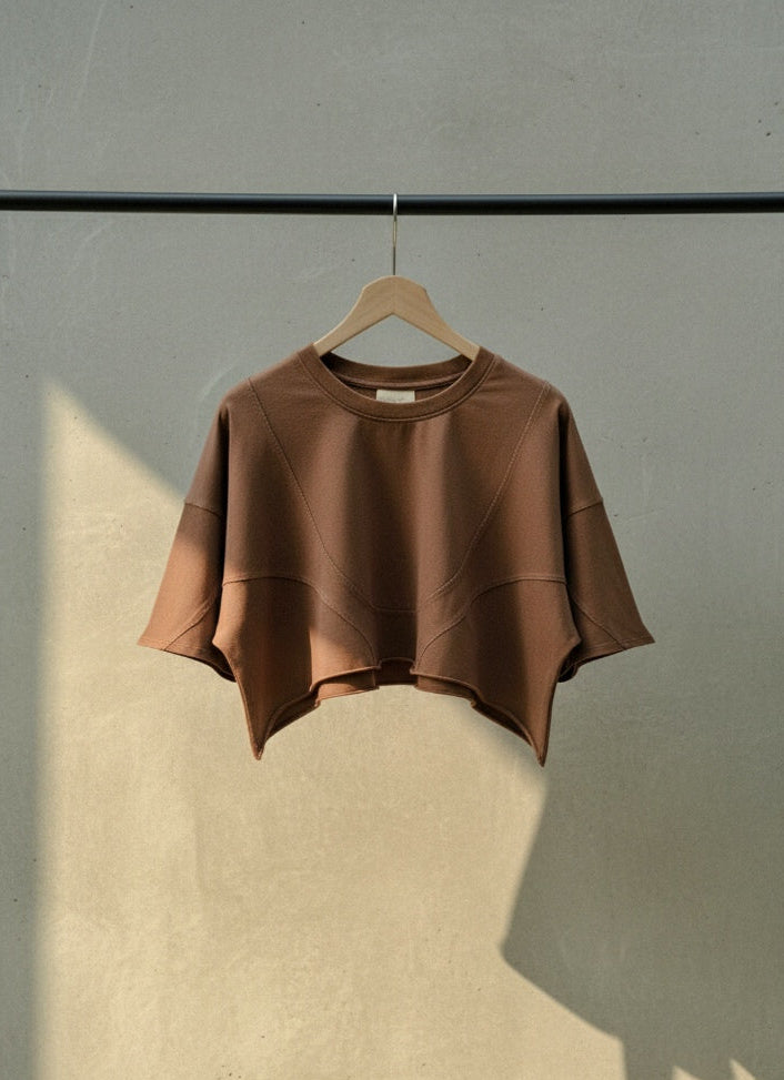 Brown crop top on a hanger against a gray wall with a light source casting a shadow.