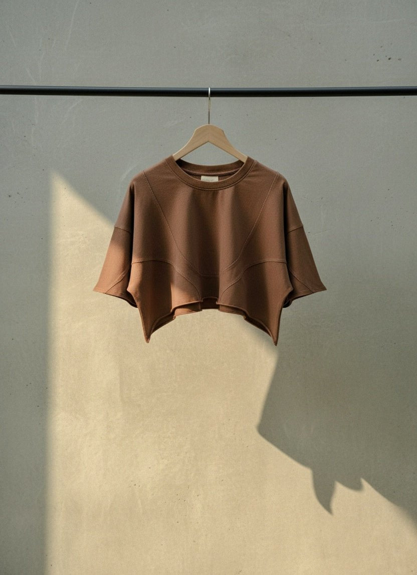Brown Vintage Linework Tee on a wooden hanger, showing its cropped shape, curved hem and linework stitching.