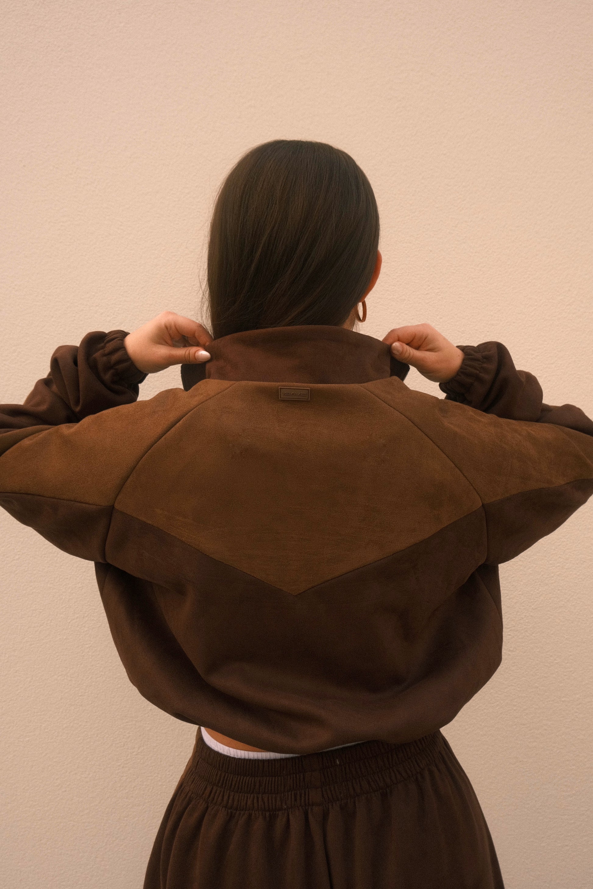 Cropped mocha brown women’s streetwear jacket with front zipper, side pockets, and unique geometric cutouts on the back – relaxed fit and soft brushed fabric.