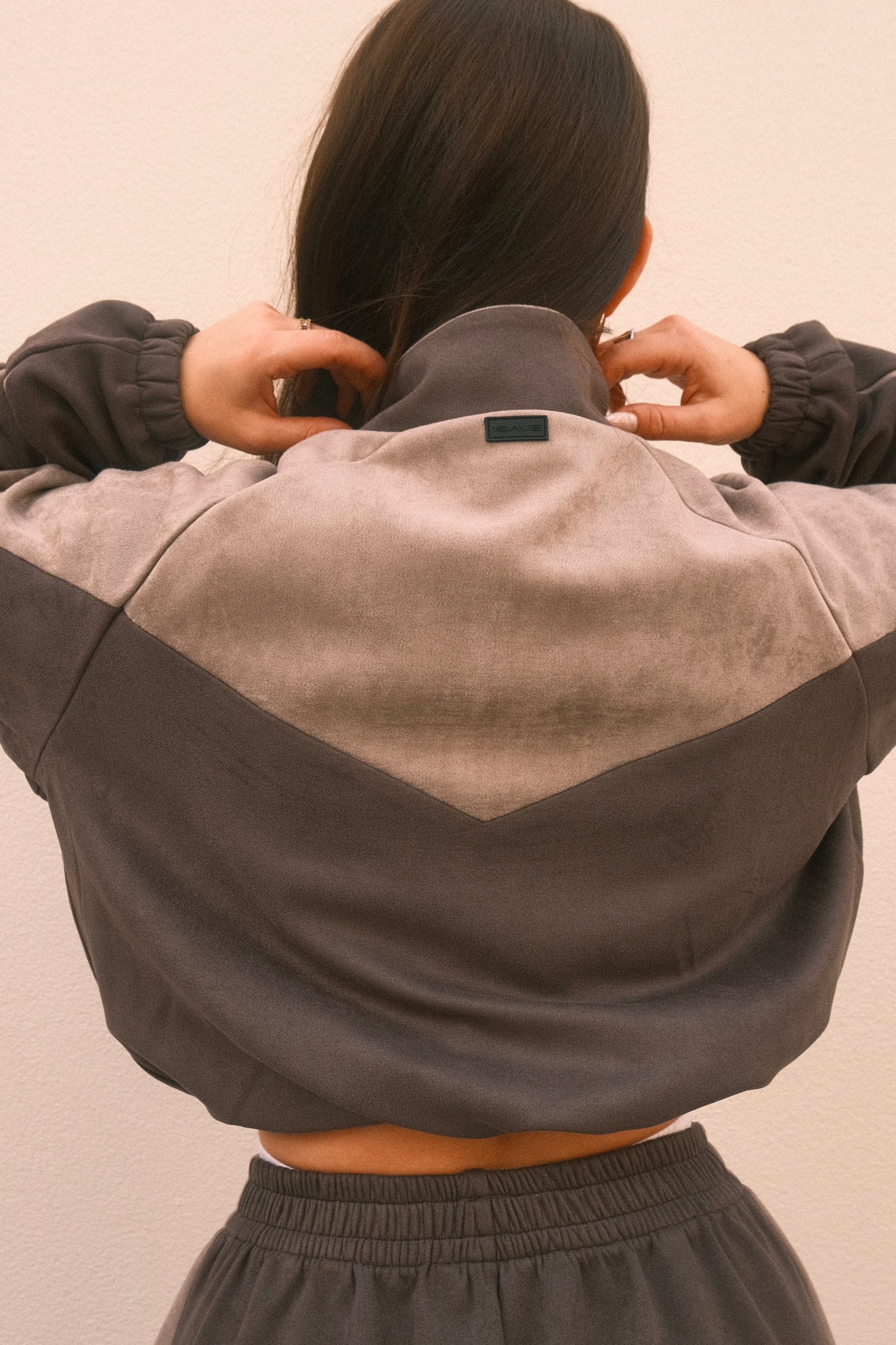 Cropped grey women’s streetwear jacket with front zipper, side pockets, and unique geometric cutouts on the back – relaxed fit and soft brushed fabric.
