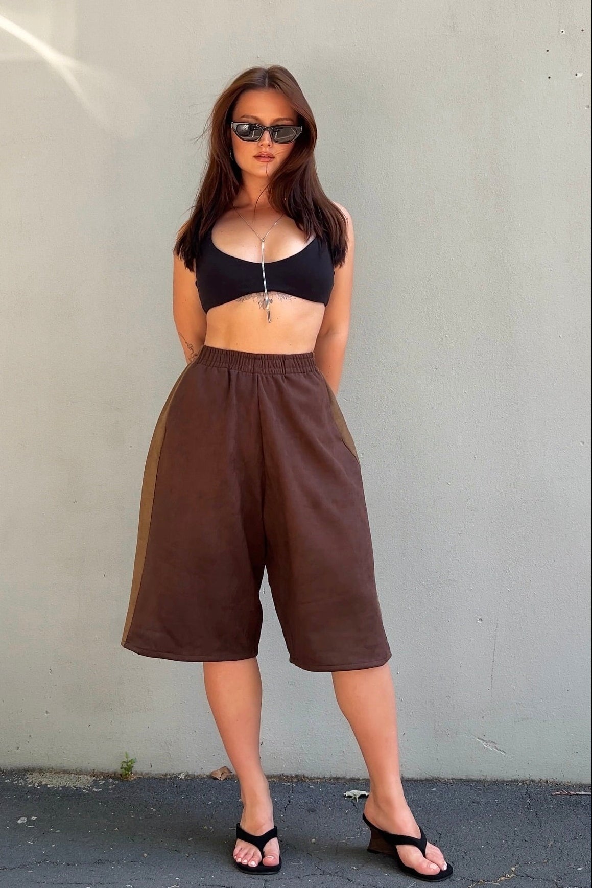 Woman wearing a black crop top and brown high-waisted pants against a plain background