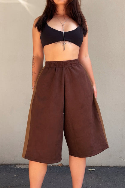 Person wearing a black crop top and brown wide-leg pants against a plain background
