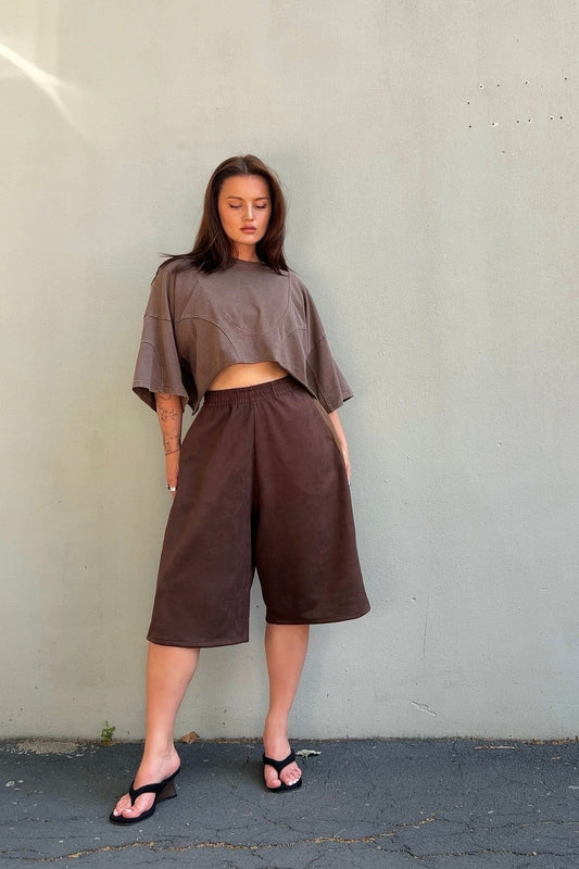 Woman wearing a brown outfit with a top and wide-leg pants against a plain background