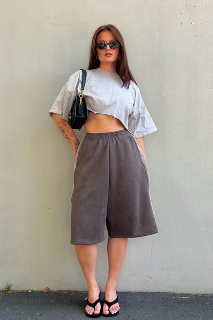 Woman wearing a white crop top and brown wide-leg pants against a plain wall.